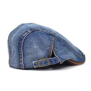 Detail of blue denim flat cap showing washed texture, contrast stitching and metal buckle