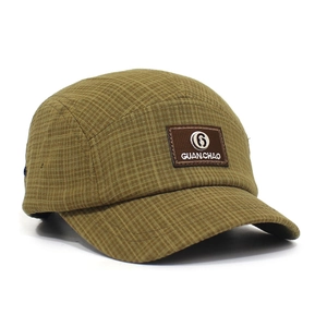 Detail van ruitjesstof en bruine leren patch op een retro groene 5-panel pet