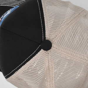 Detailed macro view of the black trucker hat featuring reinforced stitching and breathable mesh