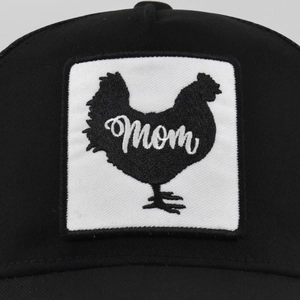 Detail van een zwarte truckerpet met vierkante patch, kip en mom-borduurwerk