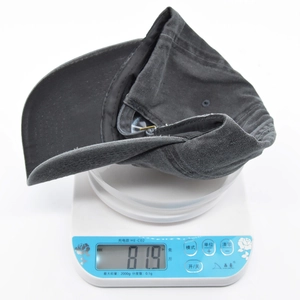 Detail of a dark gray washed cotton baseball cap weighing 81.9g on a digital scale