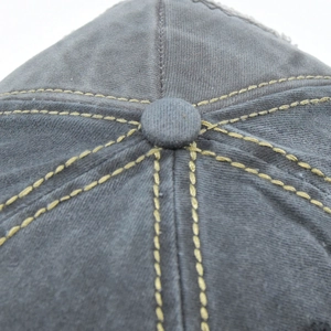 Detail view of washed grey cotton baseball cap with contrasting yellow stitching and top button