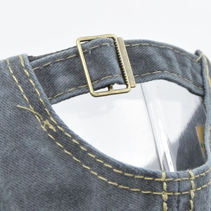 Macro view of adjustable bronze metal buckle and stitching on washed denim baseball cap