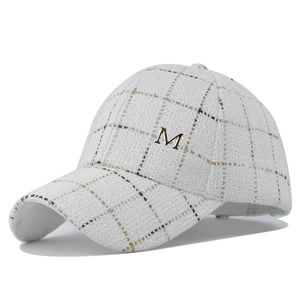 Detailed texture of white tweed baseball cap with gold metallic thread and M logo
