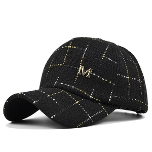 Close-up of black tweed baseball cap with gold grid pattern and metal M logo detail