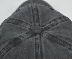 Detail view of the top button and stitching on a dark gray washed cotton baseball cap