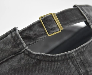 Detail view of the adjustable bronze metal buckle on a gray washed cotton military cap