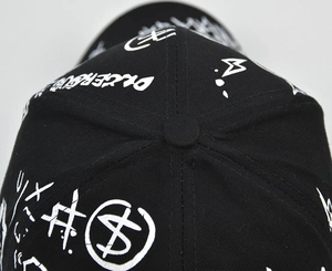 Top view detail of a black baseball cap with white graffiti patterns and top button