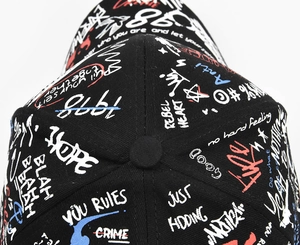 Detail view of the street graffiti patterns and text on the crown of the black baseball cap
