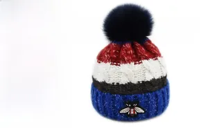 Détail du bonnet en tricot rayé avec pompon en fausse fourrure et broderie d'abeille
