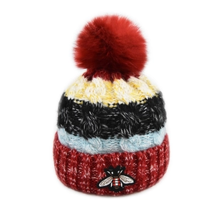 Détail d'un bonnet en tricot avec pompon en fausse fourrure et broderie abeille
