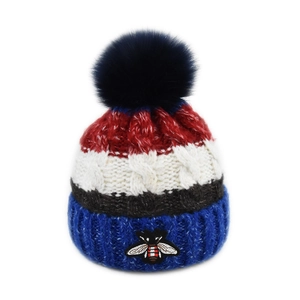 Détail d'un bonnet en tricot rayé avec broderie d'abeille et pompon en fausse fourrure