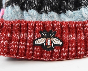Détail du bonnet en maille tricolore avec broderie d'abeille sur le revers rouge côtelé