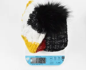 Détail du bonnet en tricot rayé sur une balance pesant 118,4 g avec pompon en fausse fourrure