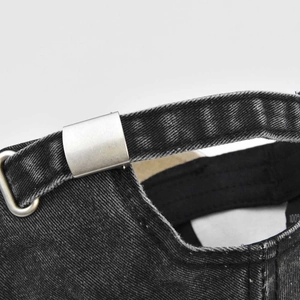 Macro detail of adjustable matte silver metal buckle on washed black denim baseball cap
