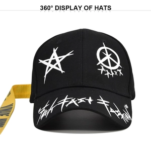 Detail of black baseball cap featuring graffiti embroidery and long yellow side strap