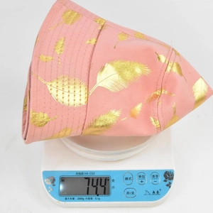 Chapeau bob rose avec feuilles dorées pesant 74,4g sur une balance pour plus de légèreté