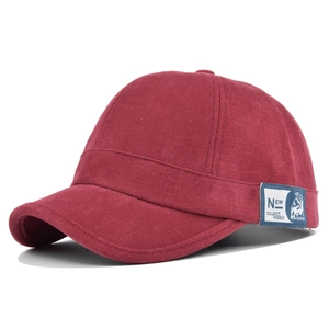 Gros plan sur la casquette bordeaux à visière courte montrant le sergé et l'écusson