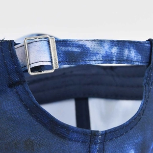 Detail of blue tie-dye baseball cap with an adjustable silver metal buckle and strap