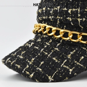 Close-up of black and gold tweed newsboy hat featuring decorative chunky metal chain