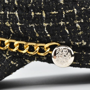 Close-up of black tweed beret with gold threads, metal chain and crest button details
