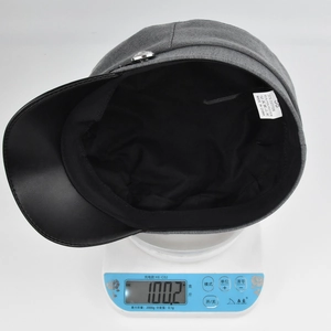 Lightweight grey newsboy cap with black leather brim weighing 100 grams on a scale