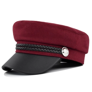 Detail of burgundy wool baker boy hat featuring a black leather brim and silver metal button
