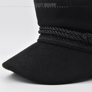Detailed close-up of a black wool baker boy hat with braided rope and elegant trim