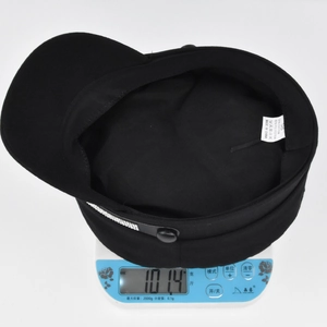 Detailed shot of a black newsboy hat on a scale showing a lightweight of 101.4g