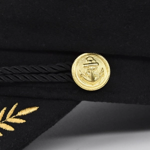 Détail du bouton ancre doré et de la broderie de blé sur une casquette de marin noire