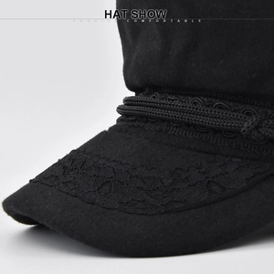 Détail d'une casquette gavroche en laine noire avec dentelle délicate et cordon tressé chic