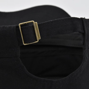 Detail of adjustable bronze metal buckle and cotton twill texture on a black cap