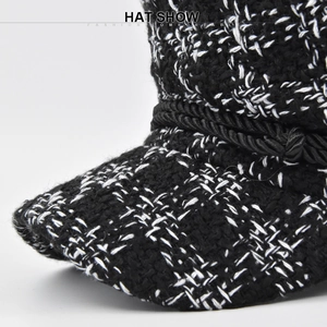 Detailed close-up of black and white tweed newsboy cap with decorative rope and metal button