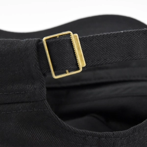 Close-up of black cotton baseball cap showing bronze metal buckle and adjustable strap