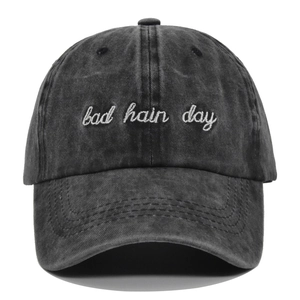 Detail of white cursive Bad Hair Day embroidery on a washed grey cotton baseball cap