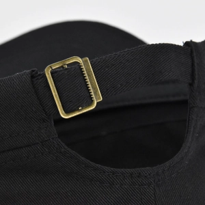 Adjustable back strap of a black cotton baseball cap with vintage brass metal buckle