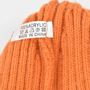 Detail showing the 100% acrylic material tag and care labels on an orange knit beanie
