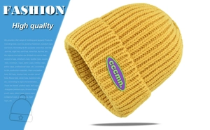 Detail of a bright yellow knitted beanie with a purple cccmn. logo patch and folded cuff