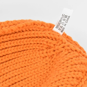 Macro shot of orange knitted hat texture showing 100% acrylic fabric label and stitching