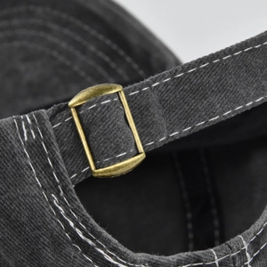 Detail of adjustable bronze metal buckle and contrast stitching on washed cotton baseball cap