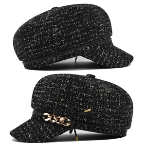 Détail d'une casquette gavroche en tweed noir avec fil doré et chaîne métallique chic