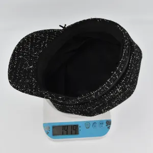 Détail montrant le poids de la casquette gavroche en tweed noir à fils argentés