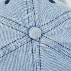 Macro detail of the light blue denim fabric stitching and top button on a baseball cap