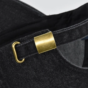 Détail de la boucle en métal bronze et du tissu denim noir sur la casquette de baseball