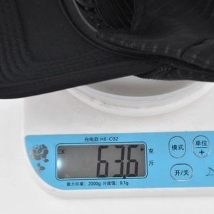Detailaufnahme einer schwarzen Baseballkappe auf einer Waage mit 63,6 Gramm Gewicht