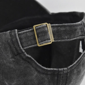 Detailed close-up of adjustable bronze metal buckle on washed black cotton baseball cap