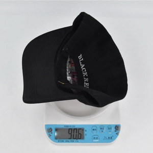 Detailaufnahme der Gewichtsmessung einer schwarzen Basecap mit 3D-Stickerei in Weiß