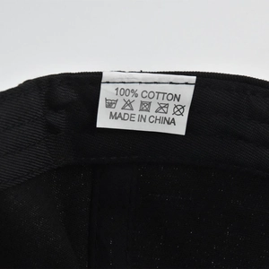 Detailed view of the 100% cotton material tag and care instructions on a black baseball cap