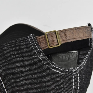 Detailed macro view of black denim baseball cap with leather strap and metal buckle