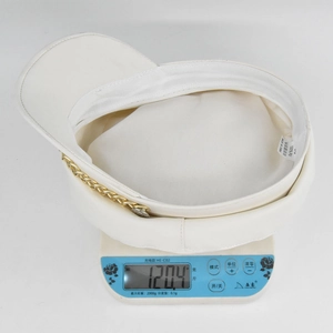Detailed top view of a white PU leather baker boy hat weighing 120.4 grams on a scale